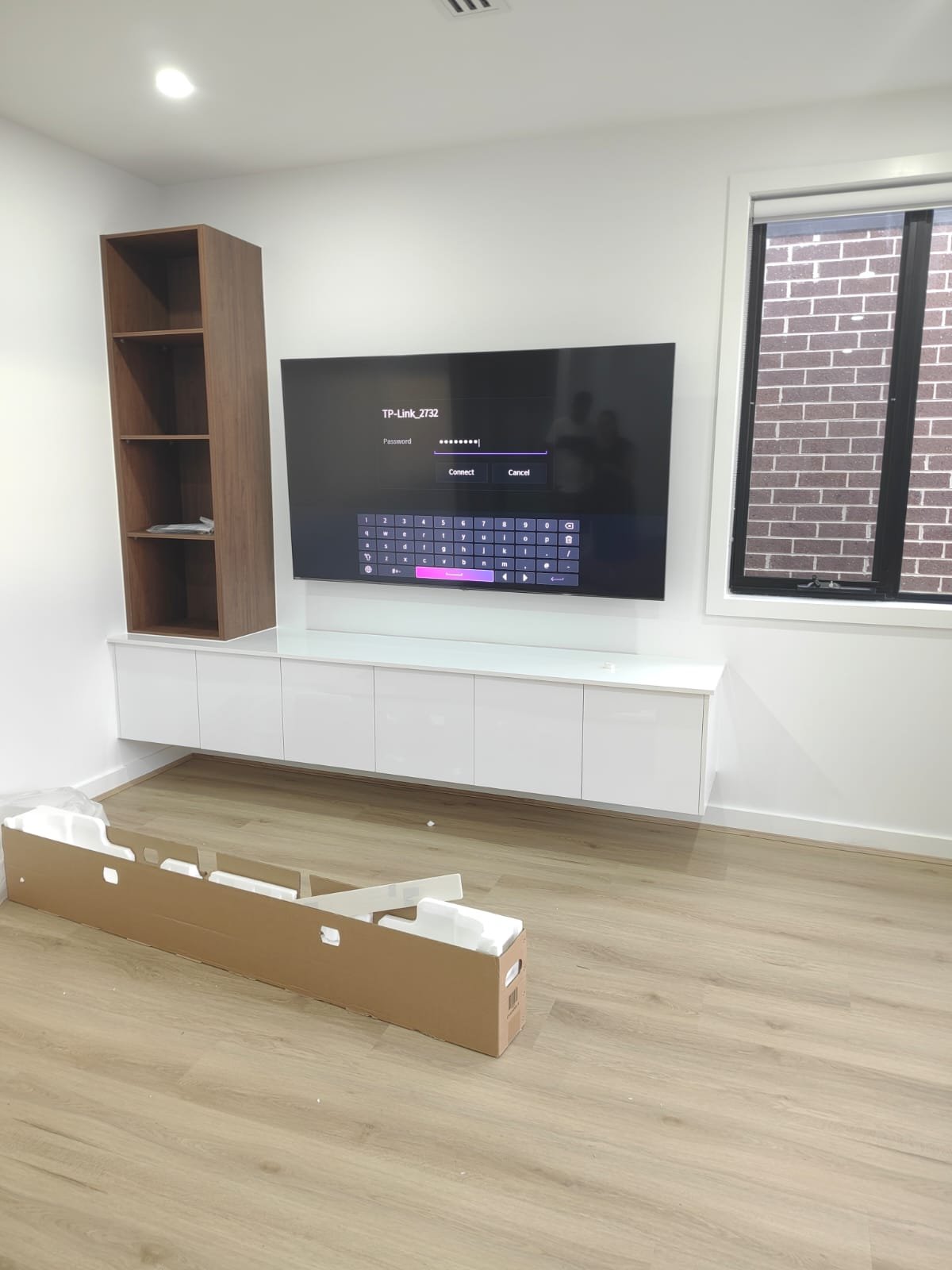 Professional TV installation with floating cabinet and wooden shelving