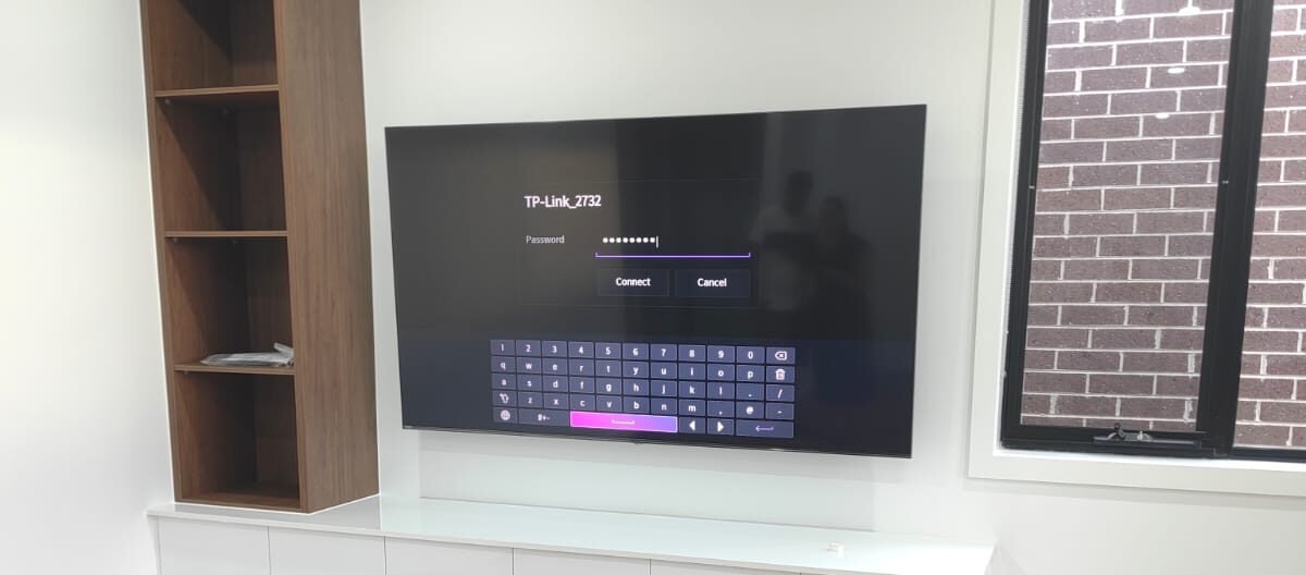 Professional TV installation with floating cabinet and wooden shelving